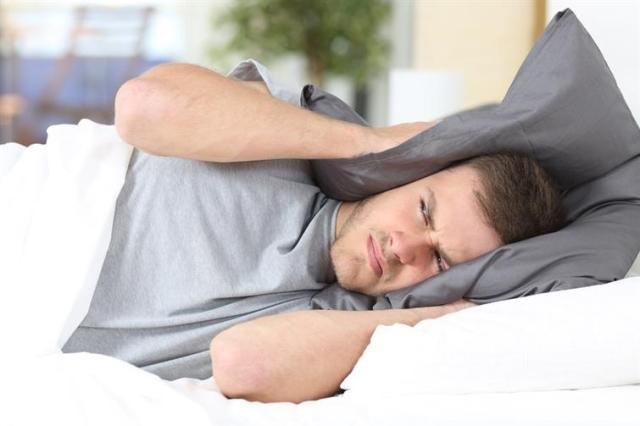 man covering his ears with a pillow showing the concept of a noisy hotel neighbour 